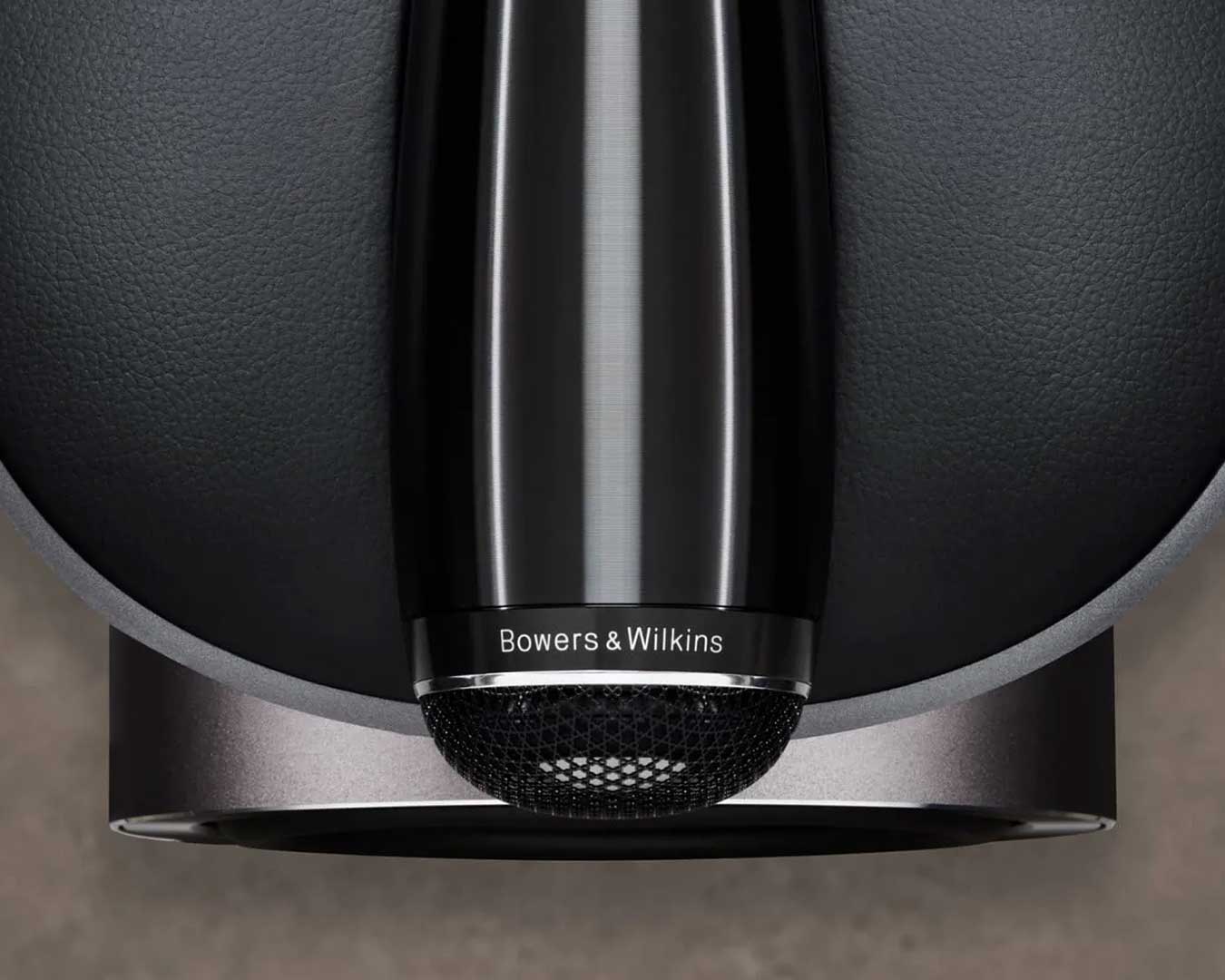 Крупный план элегантной черной акустической системы Bowers & Wilkins на текстурированном сером фоне. Глянцевая поверхность элегантно отражает свет.